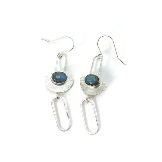 Sterling silver earrings in an art-deco geometric style. An oval labradorite stone lays horizontally across a half-circle with radial lines. The half-circle is suspended from a hook by a skinny, elongated square-wire half chain link. Below the half-circle, another elongated chainlink swing freely from a jump ring.