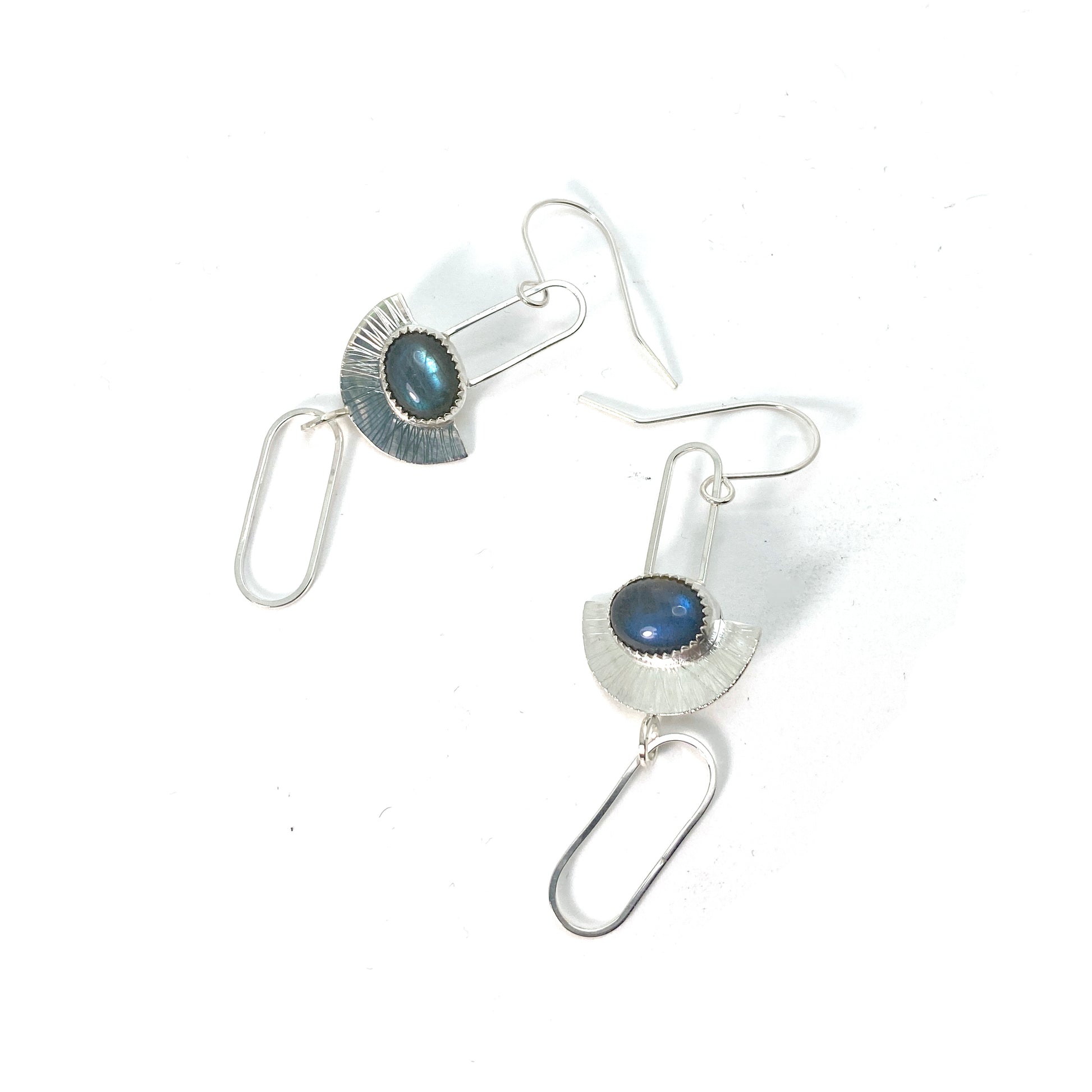 Sterling silver earrings in an art-deco geometric style. An oval labradorite stone lays horizontally across a half-circle with radial lines. The half-circle is suspended from a hook by a skinny, elongated square-wire half chain link. Below the half-circle, another elongated chainlink swing freely from a jump ring.